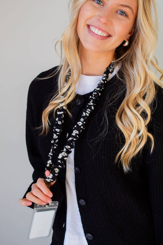 Doodlations Coffee Bar & Boutique black and white floral polyester lanyard worn by a smiling woman in a black cardigan