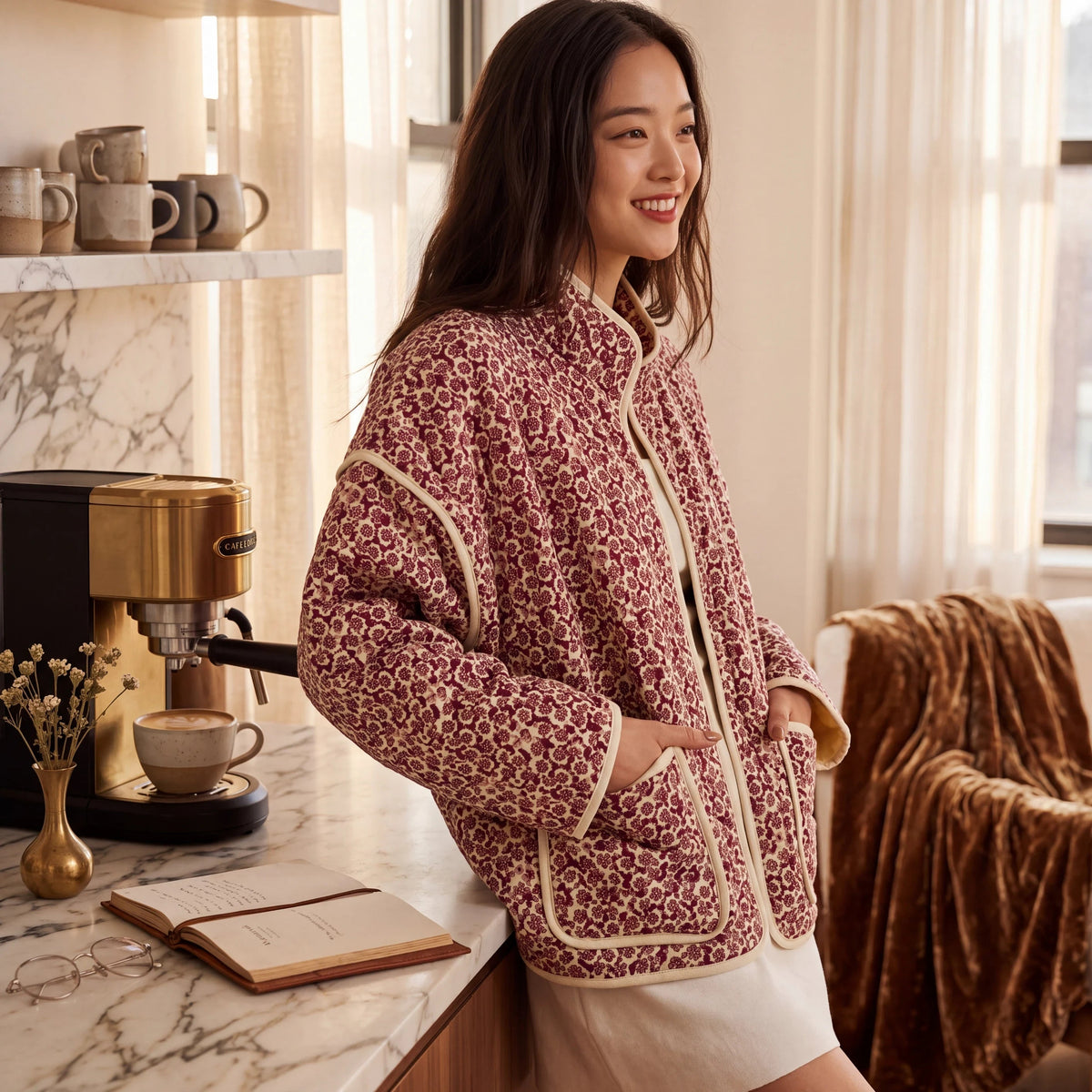 Doodlations Coffee Bar & Boutique floral quilted zip-up jacket with cream piping worn by a woman in a kitchen.