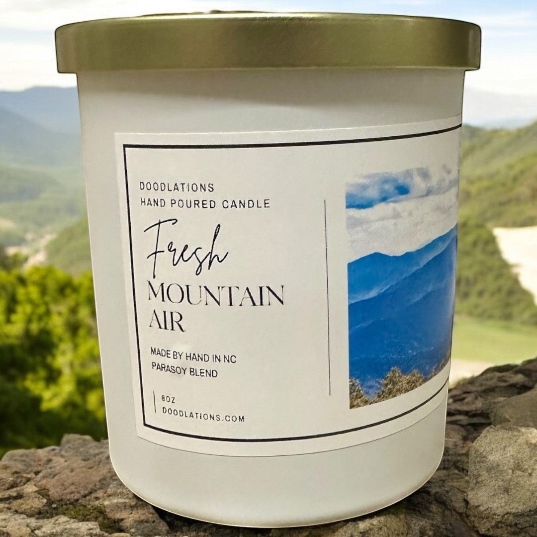Doodlations Coffee Bar & Boutique Fresh Mountain Air hand-poured soy blend candle in a white jar with a gold lid.