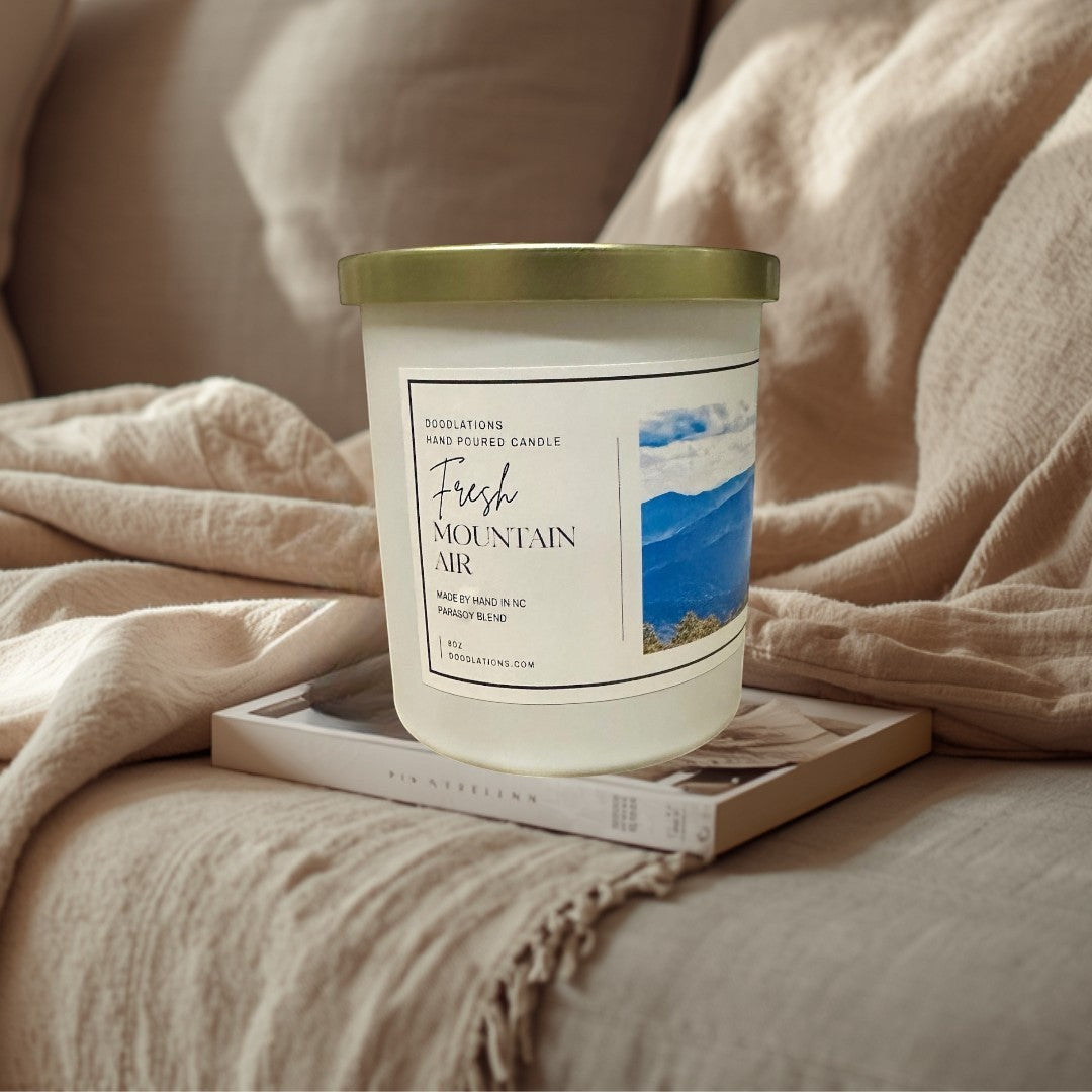 Doodlations Coffee Bar & Boutique Fresh Mountain Air luxury hand-poured soy blend candle in white jar with gold lid.