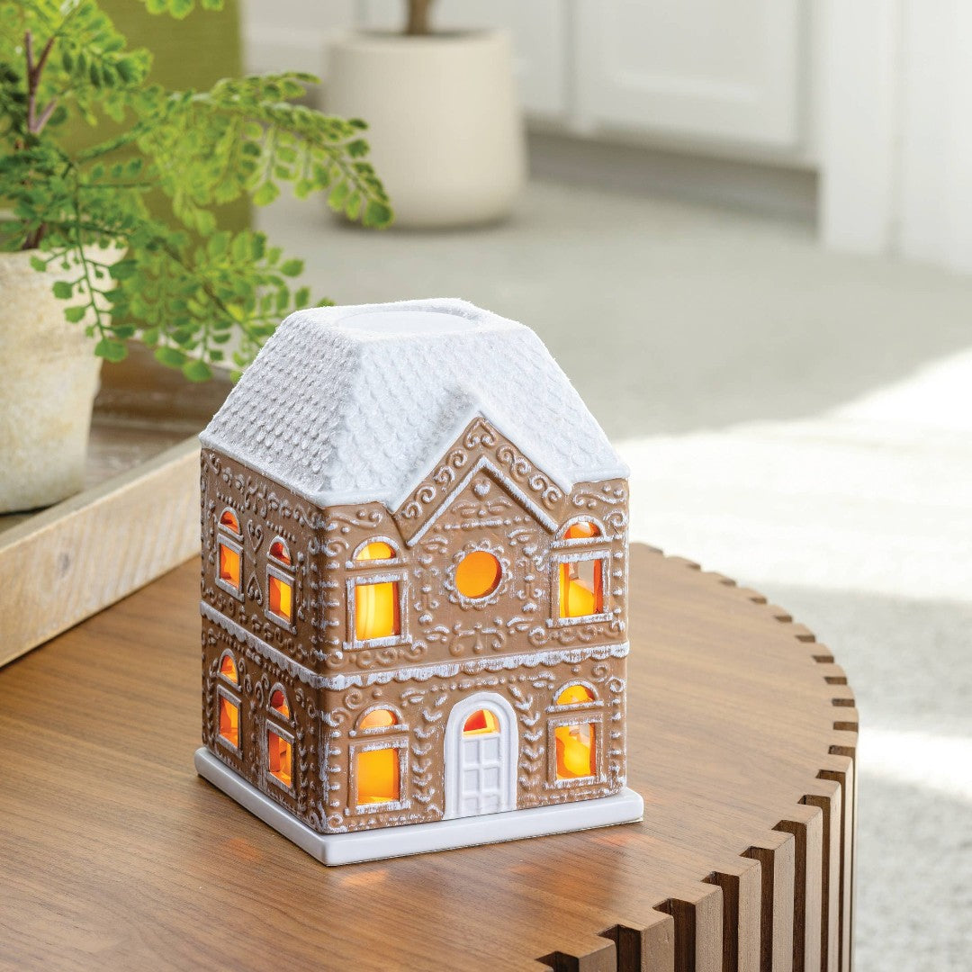 Doodlations Coffee Bar & Boutique Gingerbread House Fragrance Warmer with white snow-covered roof and illuminated windows.