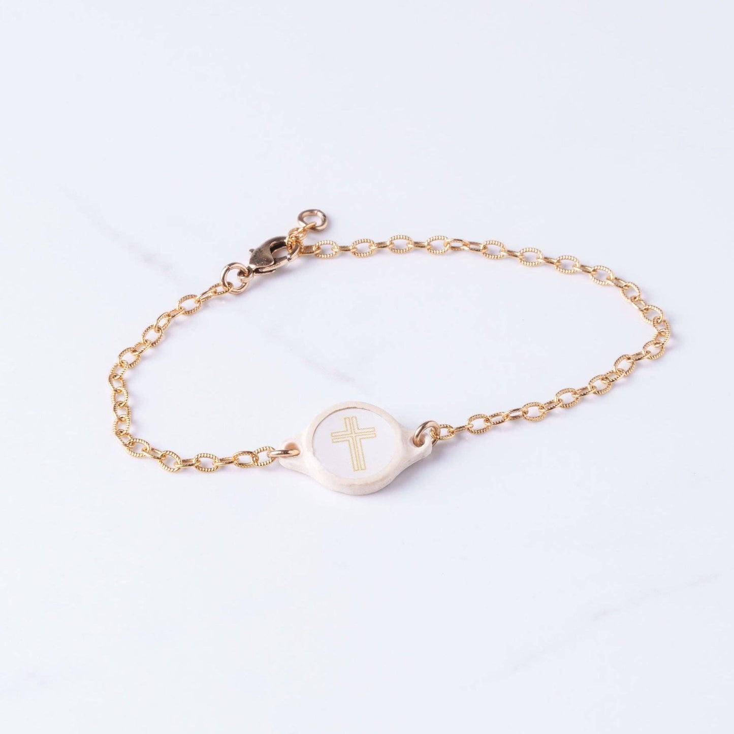 Doodlations Coffee Bar & Boutique gold chain bracelet with a cream-colored charm featuring a raised gold cross.