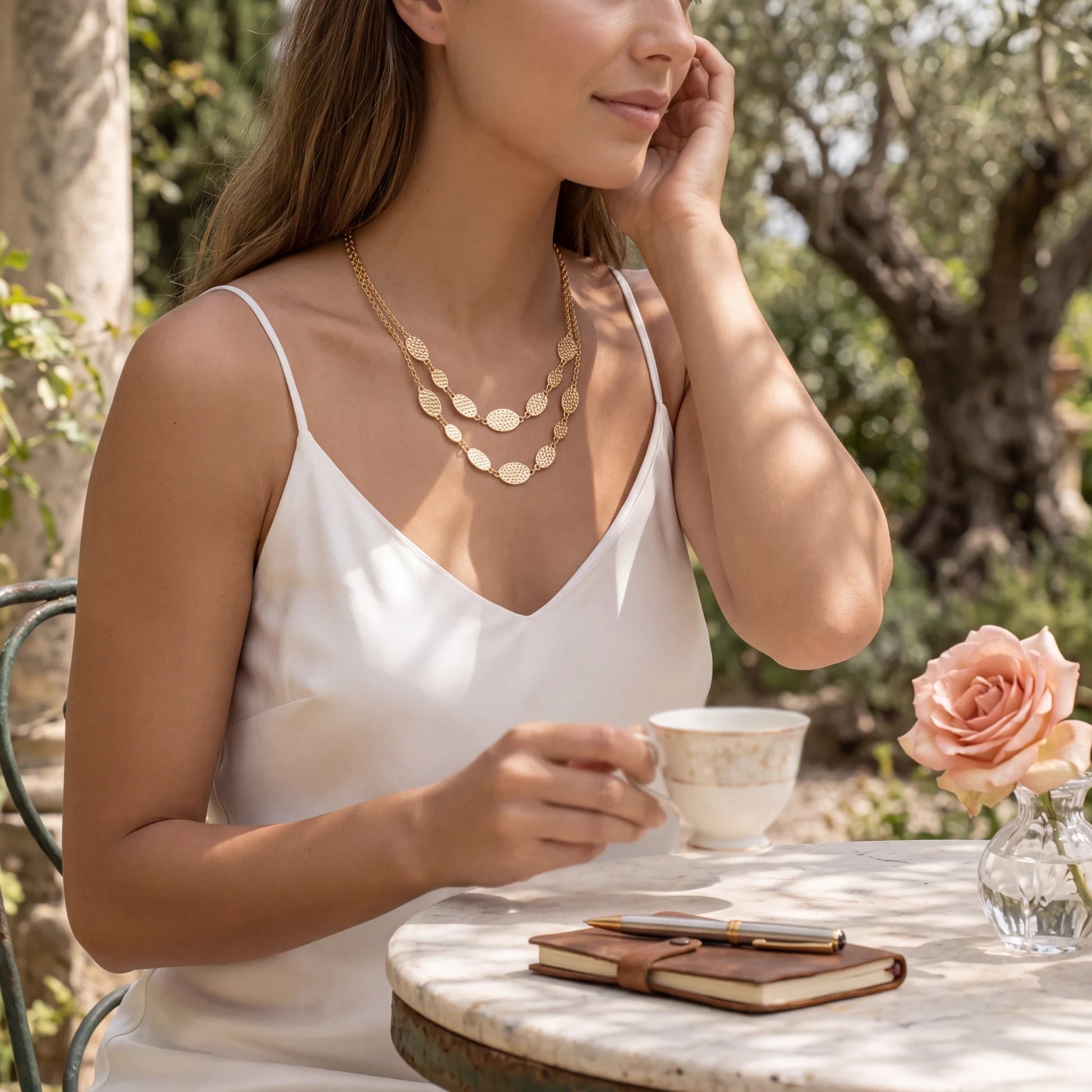 Doodlations Coffee Bar & Boutique gold-tone layered necklace with hammered oval links worn by a woman outdoors.