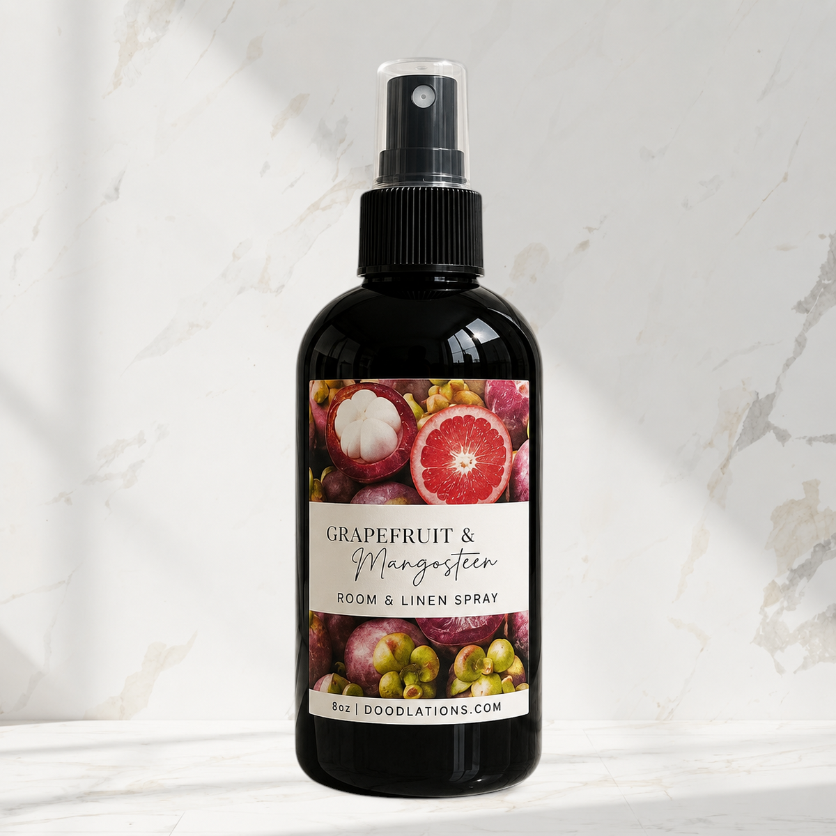 Doodlations Coffee Bar & Boutique Grapefruit & Mangosteen room and linen spray in a black bottle on a marble surface.