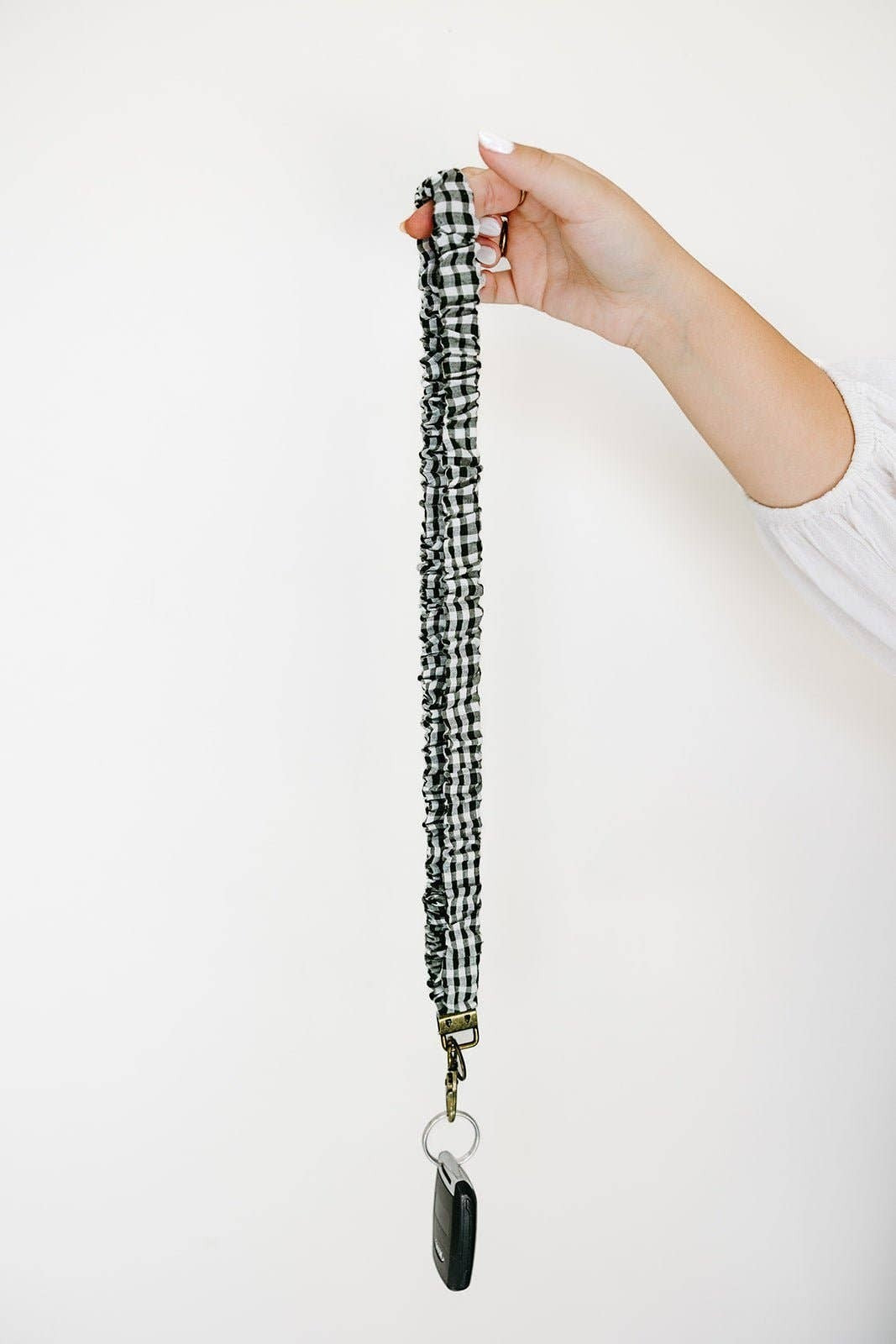 Doodlations Coffee Bar & Boutique forest green and white gingham fabric lanyard held by a hand against a white wall