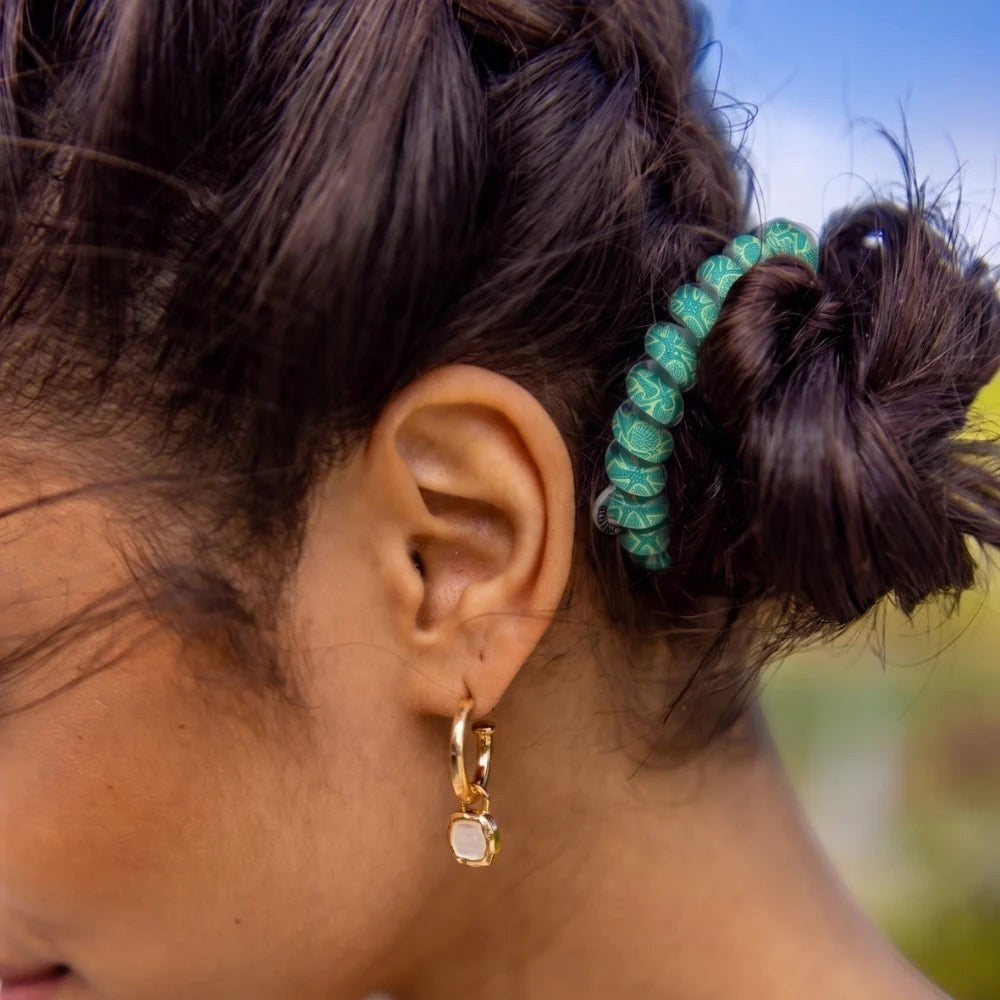 Doodlations Coffee Bar & Boutique green patterned spiral hair tie worn in a bun by a woman with gold hoop earrings