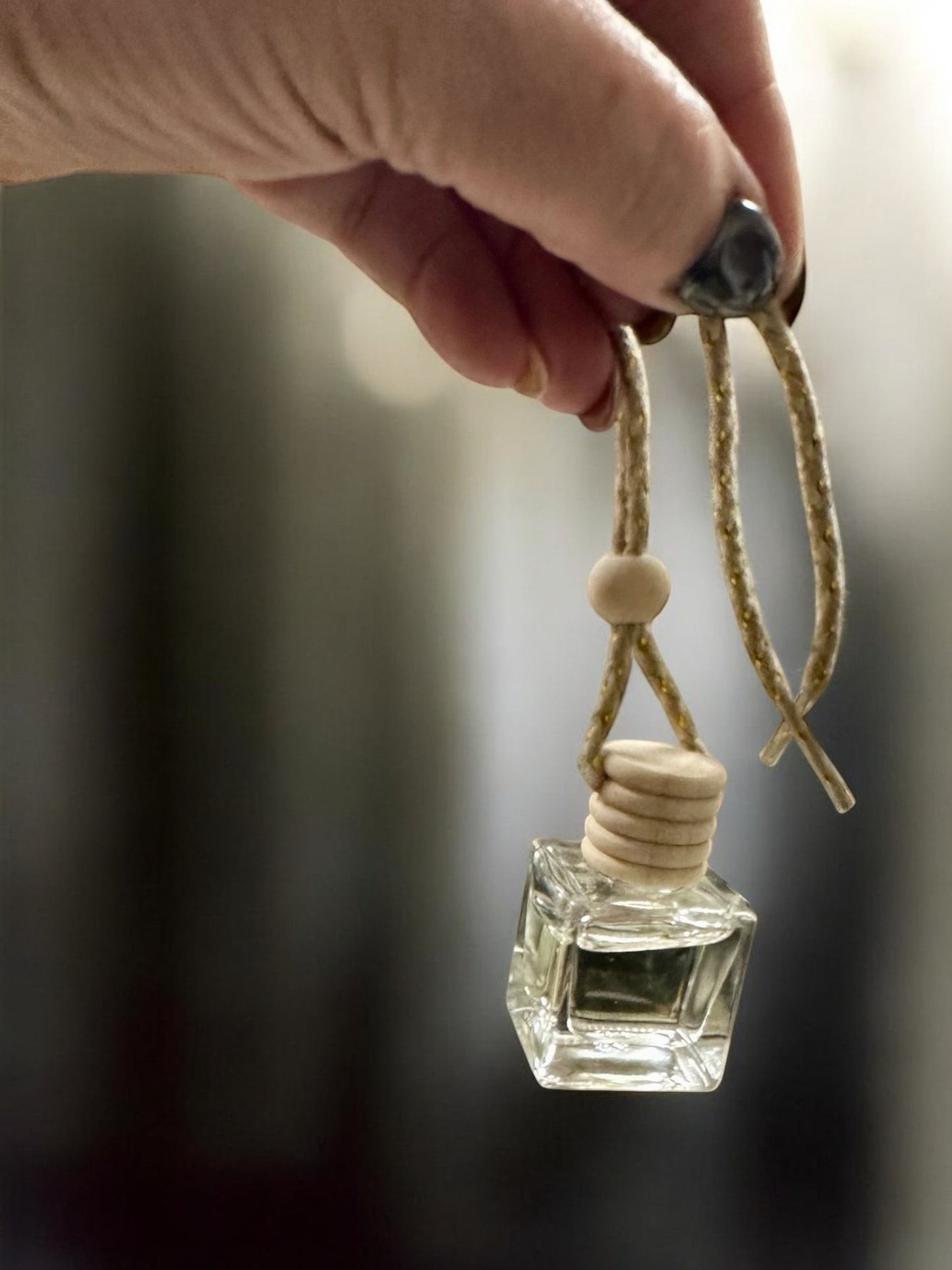 Doodlations Coffee Bar & Boutique hanging car diffuser with a clear glass bottle and wooden cap held by a hand.