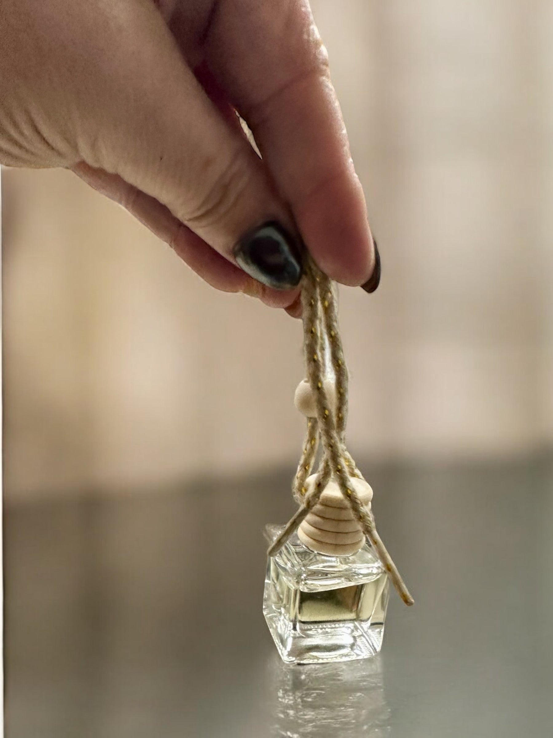 Doodlations Coffee Bar & Boutique hanging car diffuser with a glass bottle and wooden cap held by a hand.