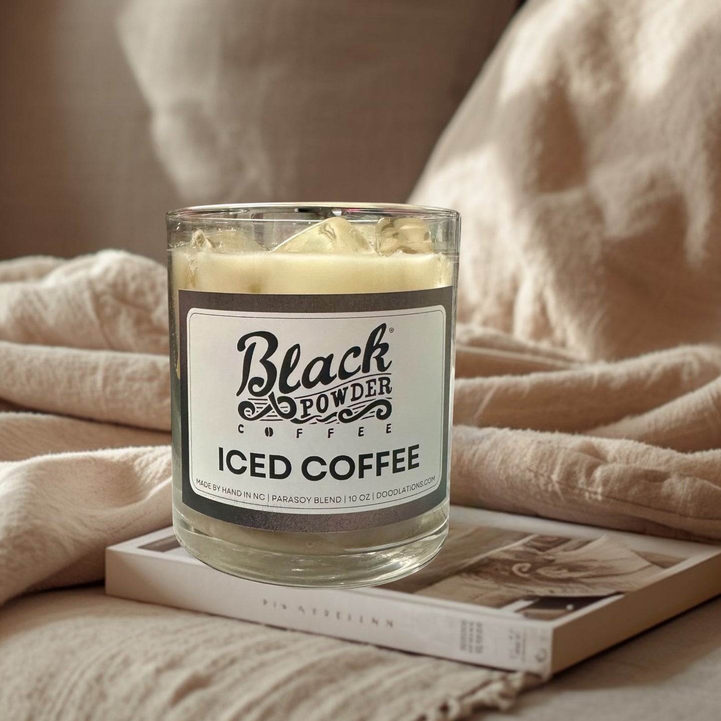 Doodlations Coffee Bar & Boutique Black Powder Iced Coffee candle in a glass jar with a creamy white wax and faux ice cubes on top.