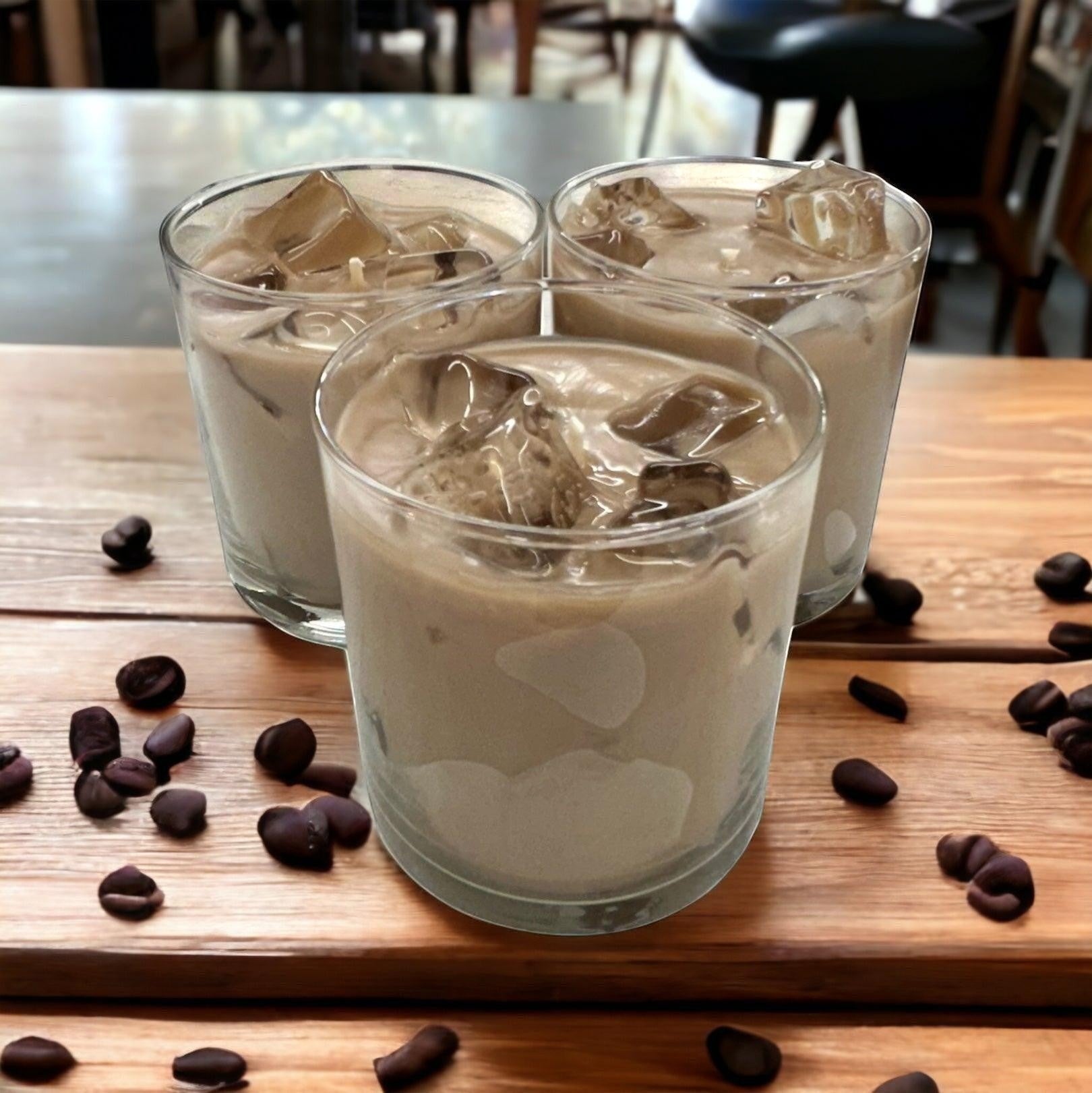 Doodlations Coffee Bar & Boutique Iced Hazelnut & Crème Coffee candle in a glass with ice cubes. Coffee beans scattered on wooden surface.