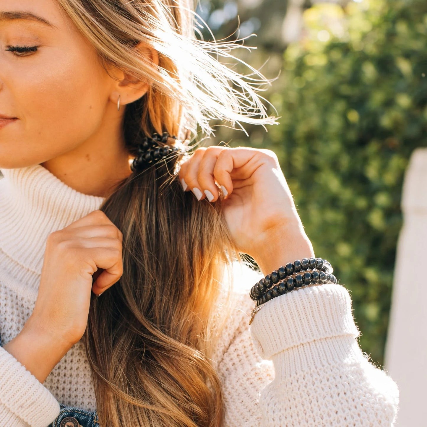 Doodlations Coffee Bar & Boutique jet black hair ties worn in hair and as a bracelet on a woman in a white sweater