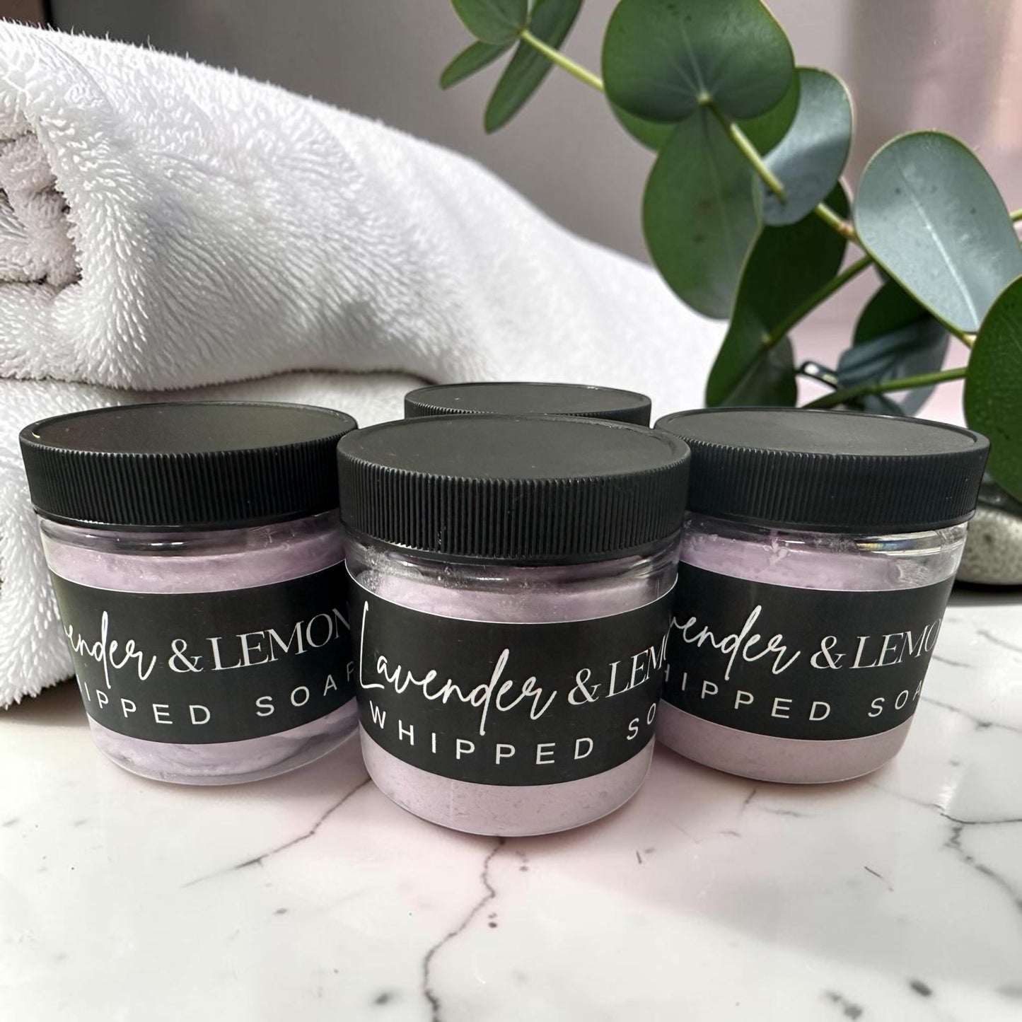 Doodlations Coffee Bar & Boutique lavender whipped soap jars with black lids on a marble surface with a white towel.