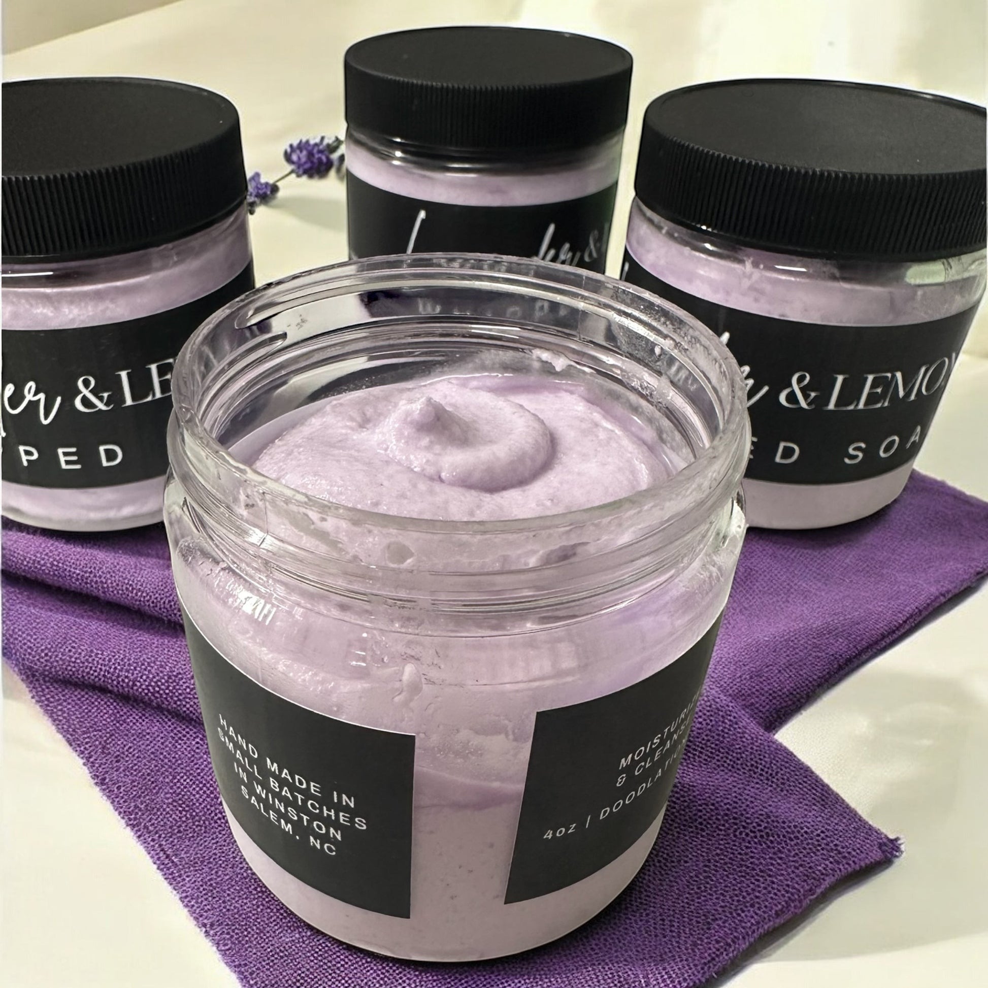 Doodlations Coffee Bar & Boutique Lavender Oasis whipped soap in 4oz jars with a light purple texture on a purple cloth.
