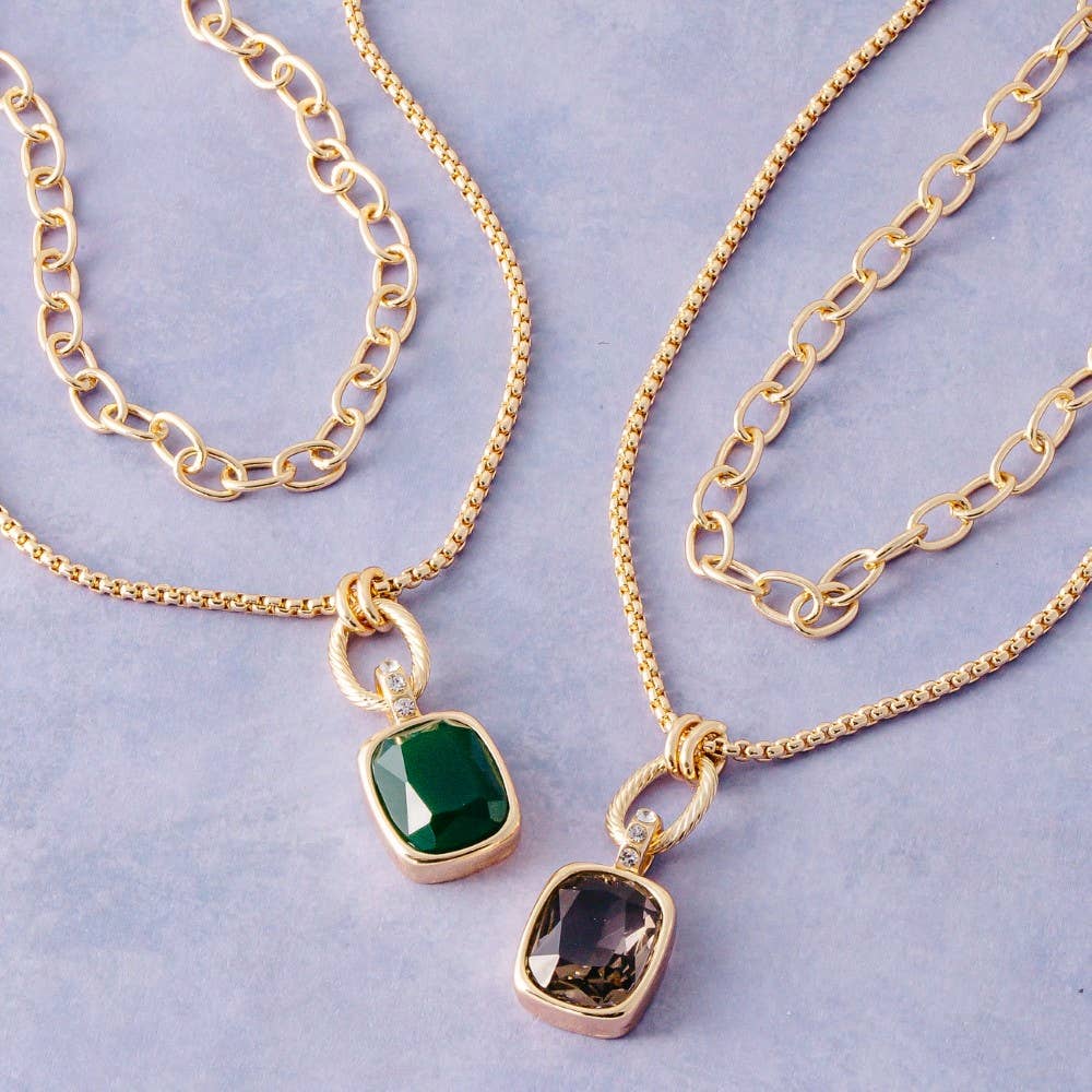 Doodlations Coffee Bar & Boutique layered gold-tone necklaces with emerald and smoky cushion-cut gemstone pendants.