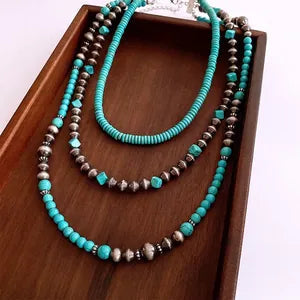 Doodlations Coffee Bar & Boutique layered necklace with turquoise beads and metallic accents on a wooden tray