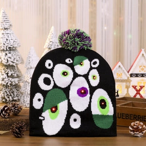 Doodlations Coffee Bar & Boutique black knit beanie with LED monster eyes and a green and purple pom-pom topper
