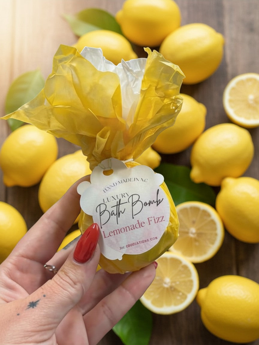 Doodlations Coffee Bar & Boutique Lemonade Fizz bath bomb wrapped in yellow paper held against a background of lemons.