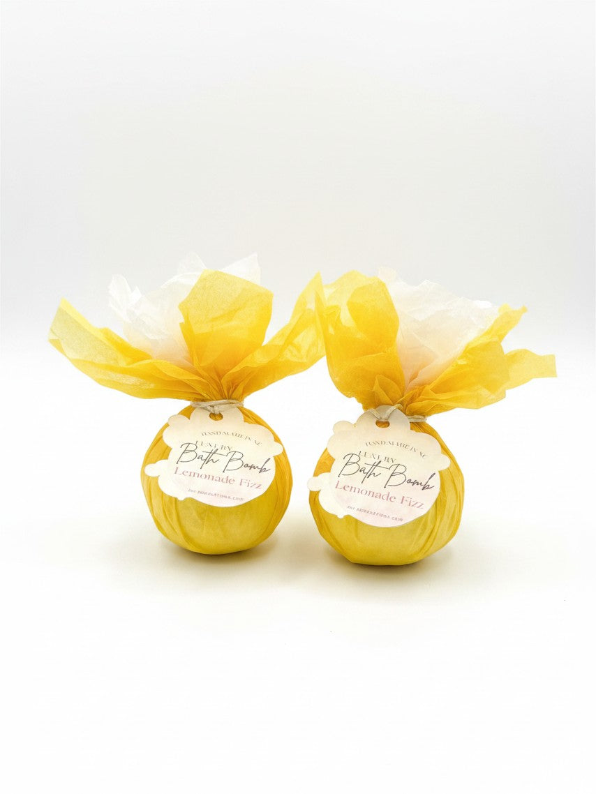 Two Doodlations Coffee Bar & Boutique Lemonade Fizz bath bombs wrapped in yellow tissue paper with branded tags.
