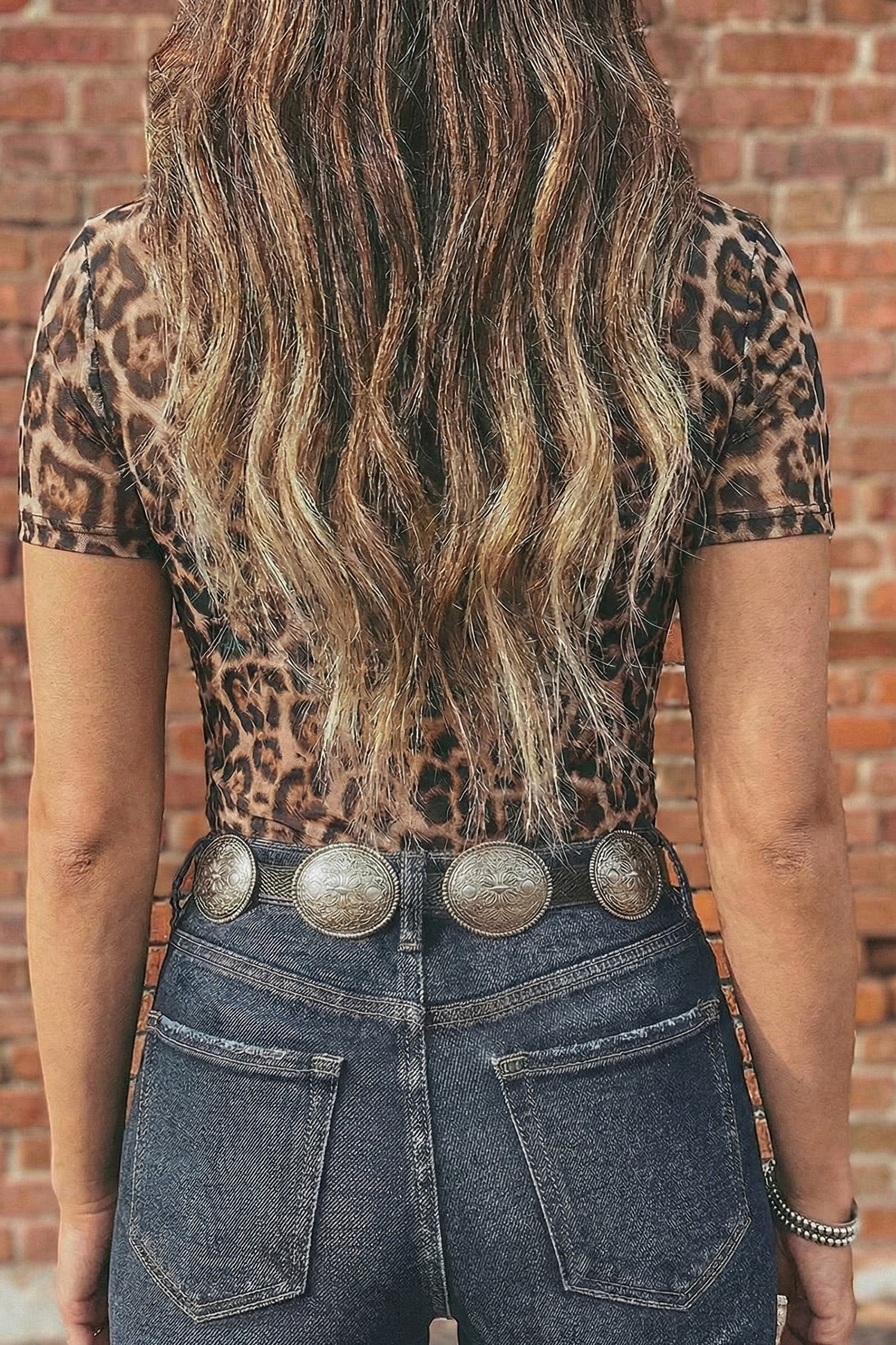 Doodlations Coffee Bar & Boutique leopard print short sleeve mesh top worn with dark denim jeans and a concho belt.