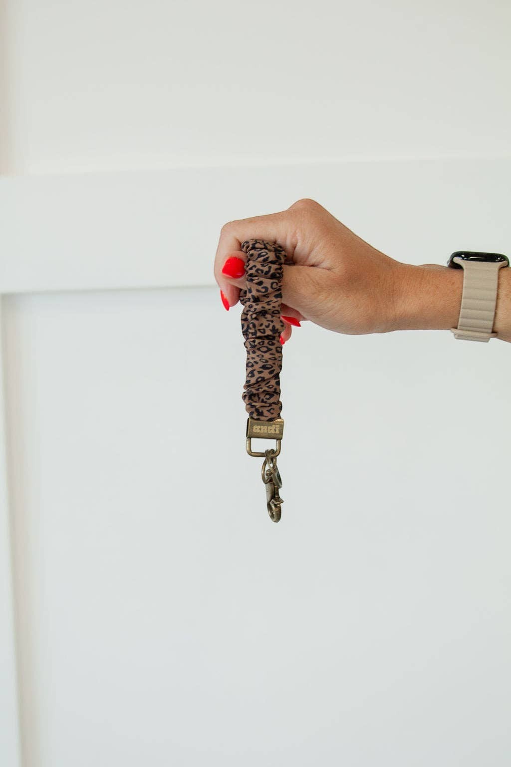 Doodlations Coffee Bar & Boutique leopard print scrunchie keychain with bronze hardware held in a hand