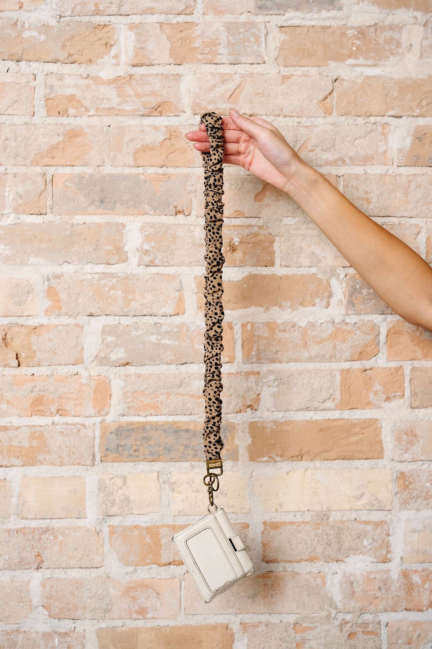Doodlations Coffee Bar & Boutique leopard print scrunchie lanyard with an attached white ID holder against brick wall