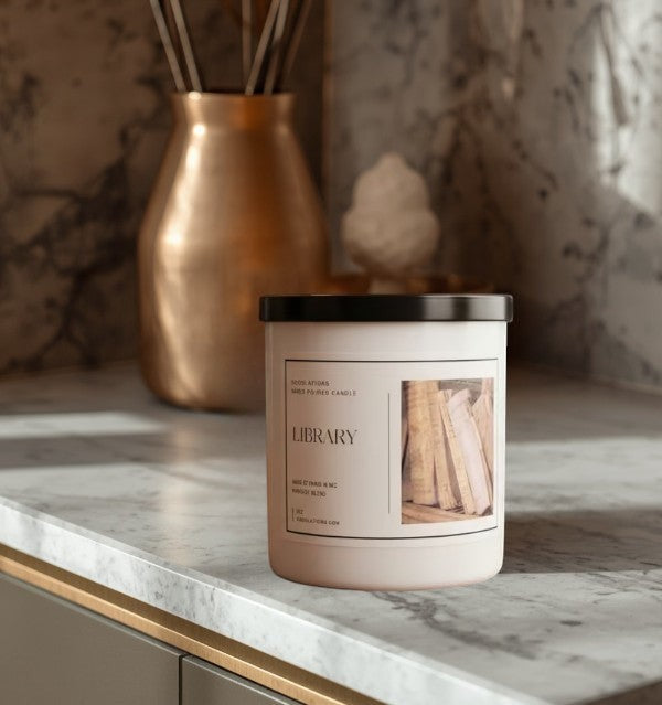 Doodlations Coffee Bar & Boutique Library luxury boutique candle with a sophisticated woodsy scent, in a white jar with a black lid.