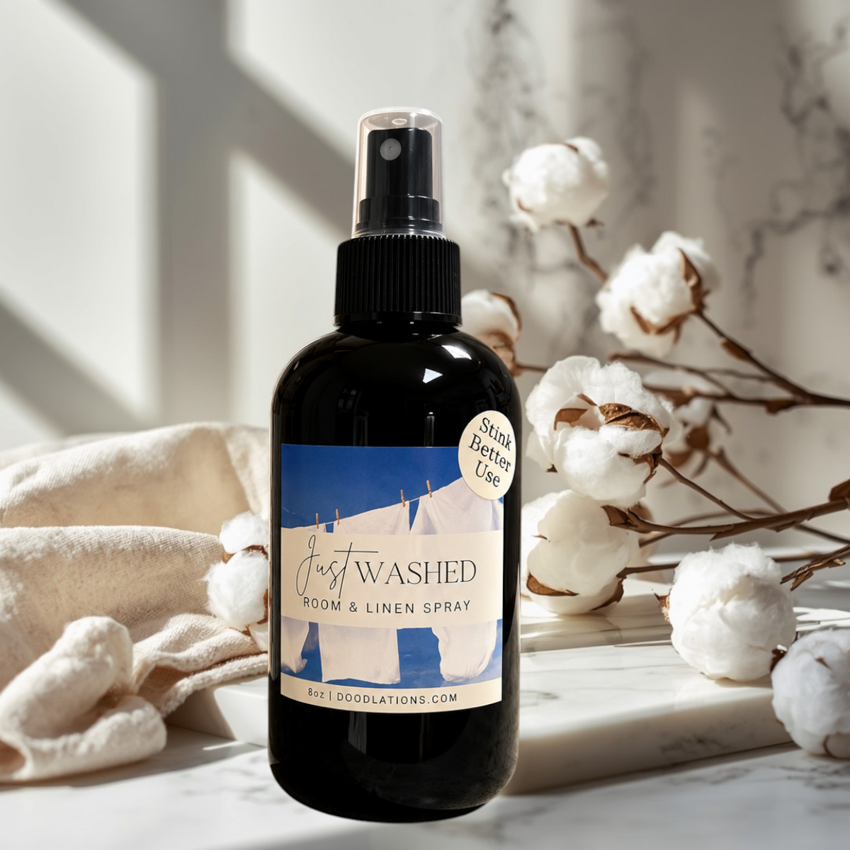 Doodlations Coffee Bar & Boutique Just Washed room and linen spray in a black bottle with cotton blossoms on marble.