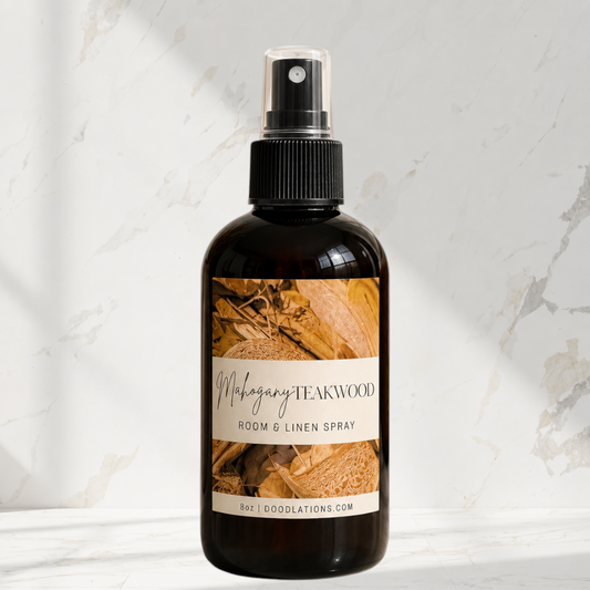 Doodlations Coffee Bar & Boutique Mahogany Teakwood room and linen spray in an amber glass bottle on marble surface.