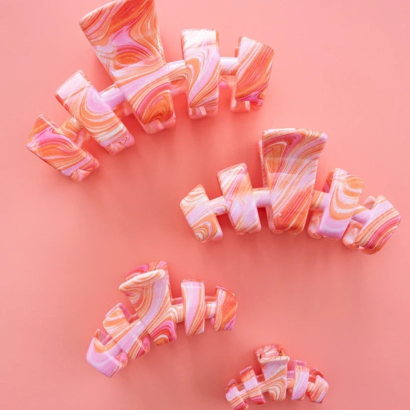Doodlations Coffee Bar & Boutique Classic Just Keep Swimming claw hair clips in a pink and orange marble swirl pattern.