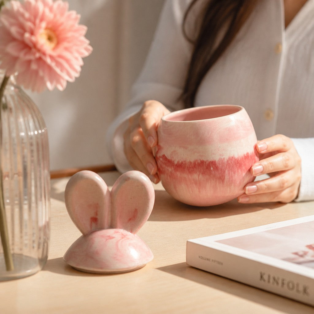 Doodlations Coffee Bar & Boutique marbled pink concrete bunny candle vessel held by a person on a wooden table.