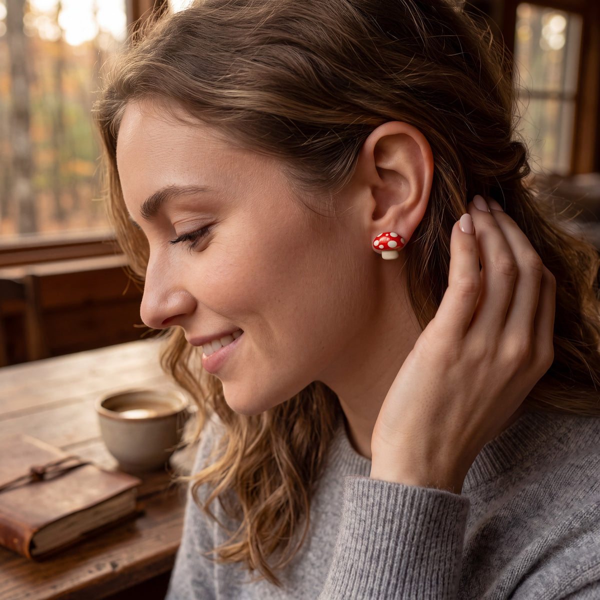 Doodlations Coffee Bar & Boutique handmade red and white mushroom stud earrings worn by a smiling woman in a cafe.