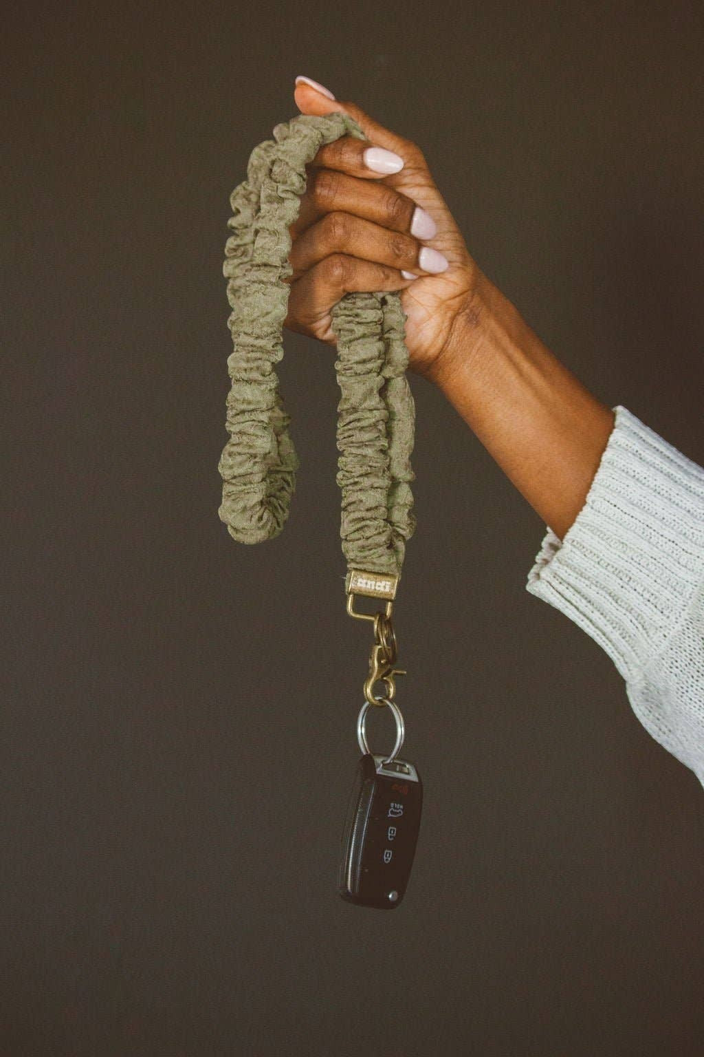 Doodlations Coffee Bar & Boutique moss green crinkled cotton fabric lanyard held in a hand with a car key attached