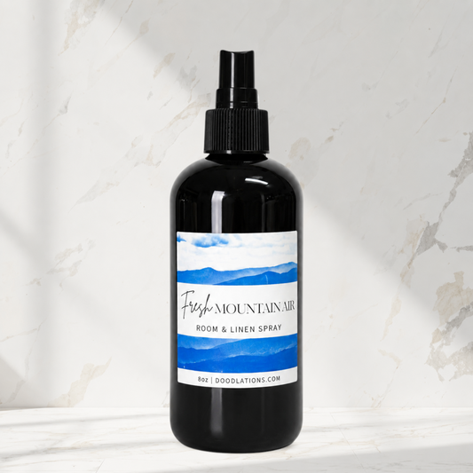Doodlations Coffee Bar & Boutique Fresh Mountain Air room and linen spray in a black 8oz bottle on a marble surface.