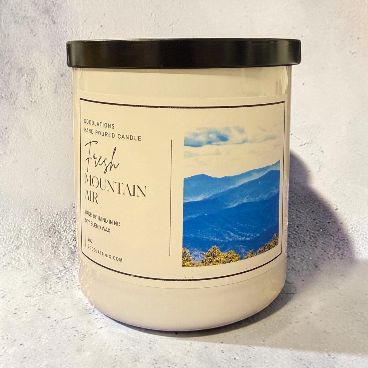 Doodlations Coffee Bar & Boutique Fresh Mountain Air luxury soy blend candle in a white jar with a black lid