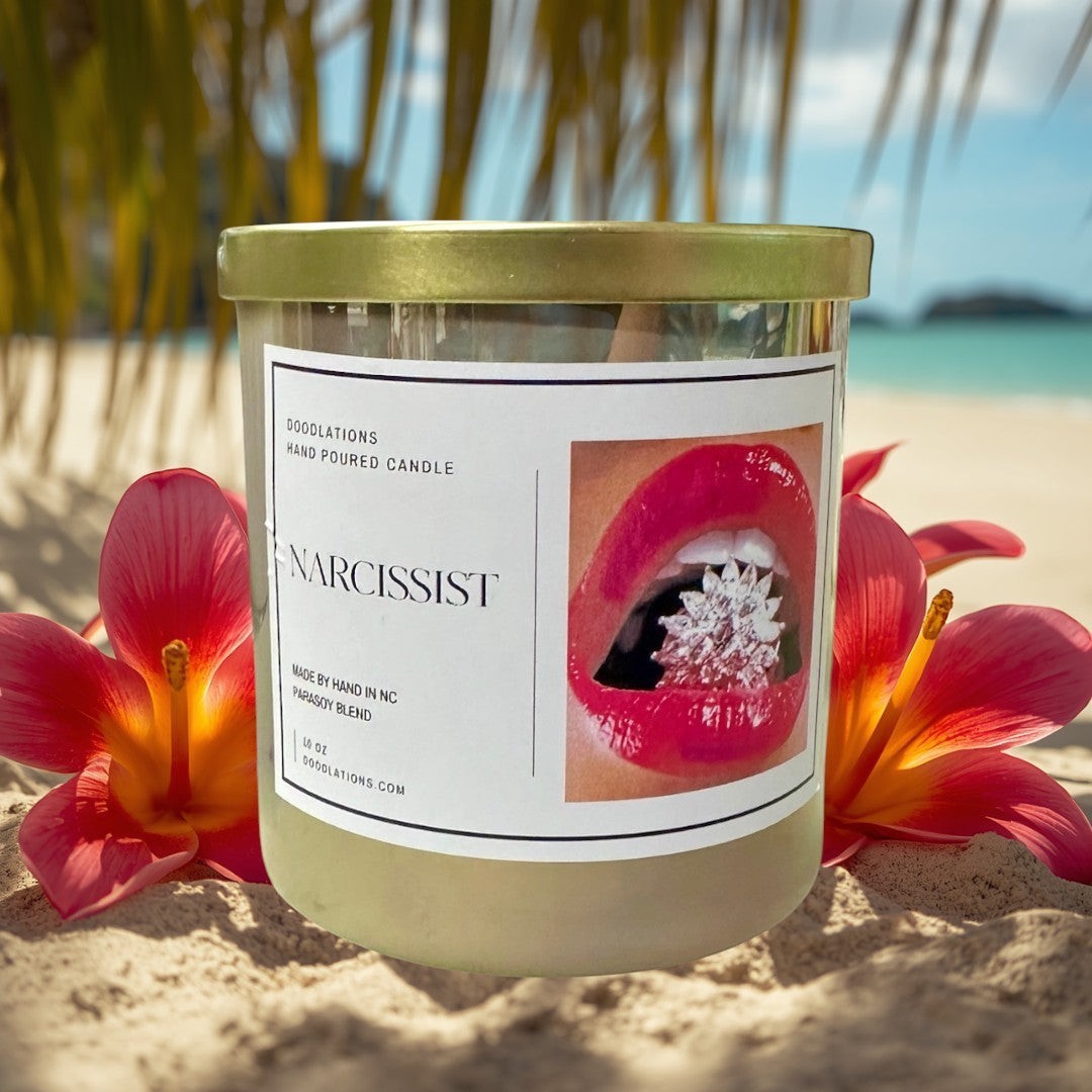 Doodlations Coffee Bar & Boutique Narcissist hand-poured soy blend candle in a clear jar with a gold lid. Features a label with red lips and a sparkling gem.