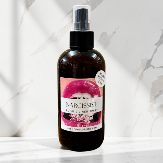 Doodlations Coffee Bar & Boutique Narcissist room and linen spray in an amber bottle with a vibrant lip graphic label.