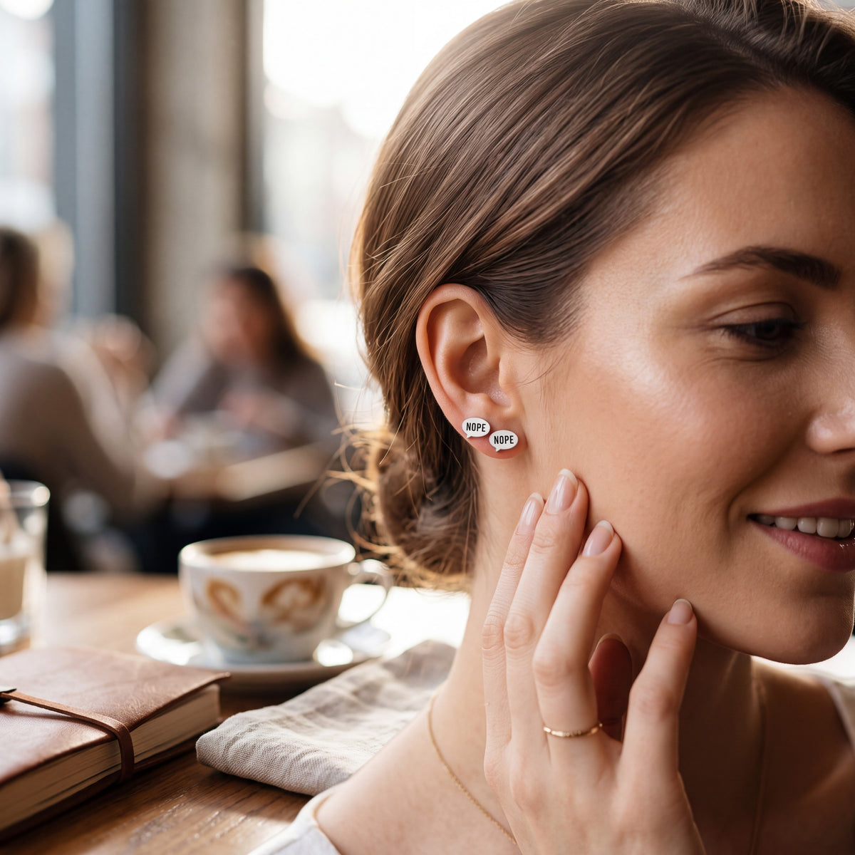 Doodlations Coffee Bar & Boutique Nope earrings featuring speech bubble designs worn by a woman in a cafe setting