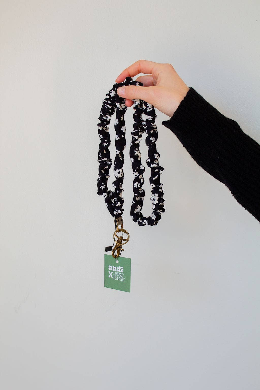 Doodlations Coffee Bar & Boutique black and white floral polyester lanyard with brass hardware held by a hand