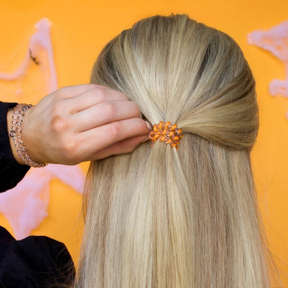 Doodlations Coffee Bar & Boutique orange sparkly hair tie securing a half-up hairstyle on blonde hair