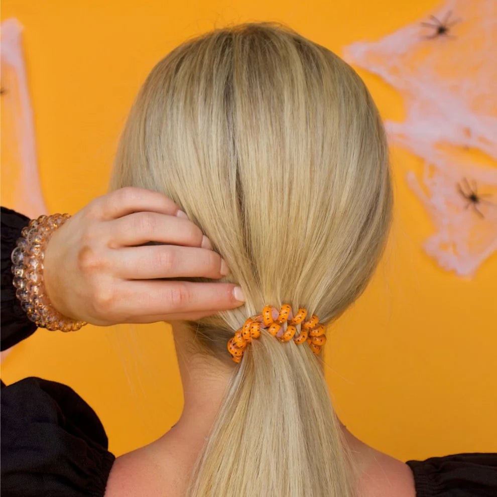 Doodlations Coffee Bar & Boutique orange spiral hair tie on blonde ponytail against a spooky Halloween background