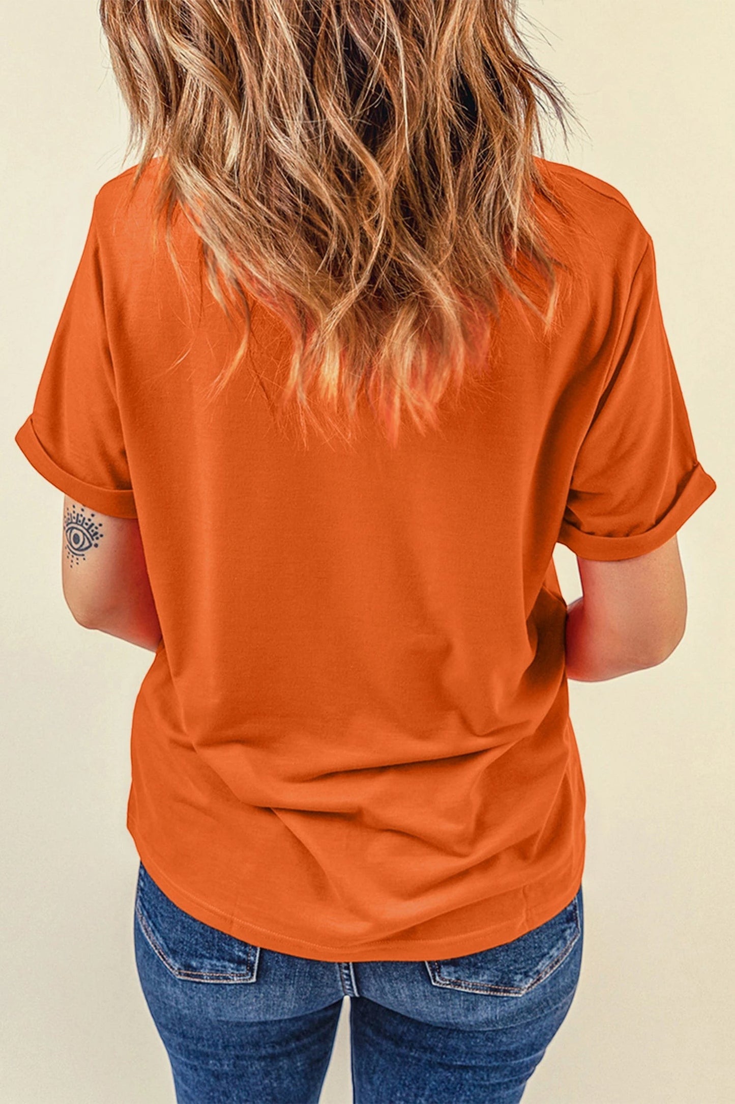 Back view of a woman wearing a vibrant orange Doodlations Coffee Bar & Boutique t-shirt with cuffed sleeves.