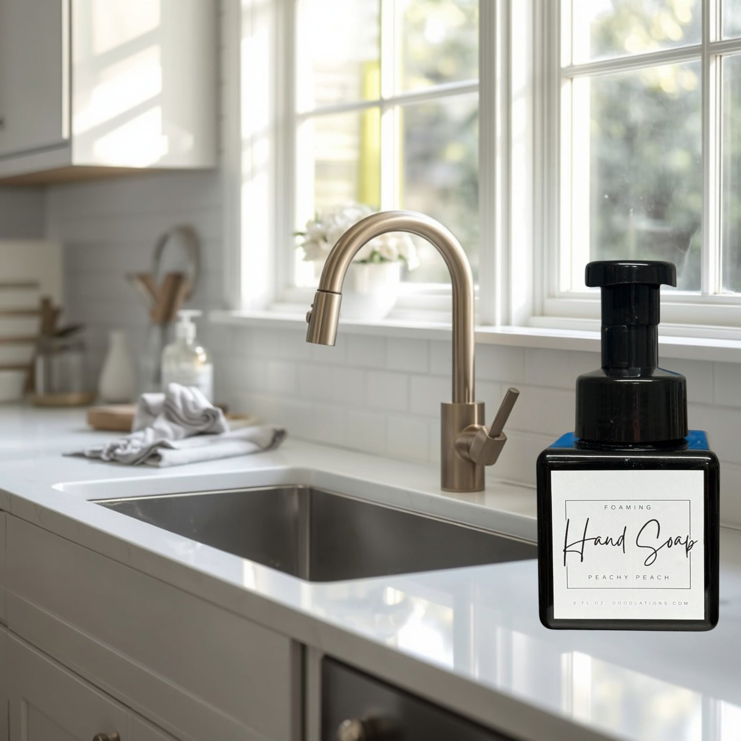 Doodlations Peachy Peach foaming hand soap in a black square bottle with a black pump dispenser. Surrounded by green artificial plants.