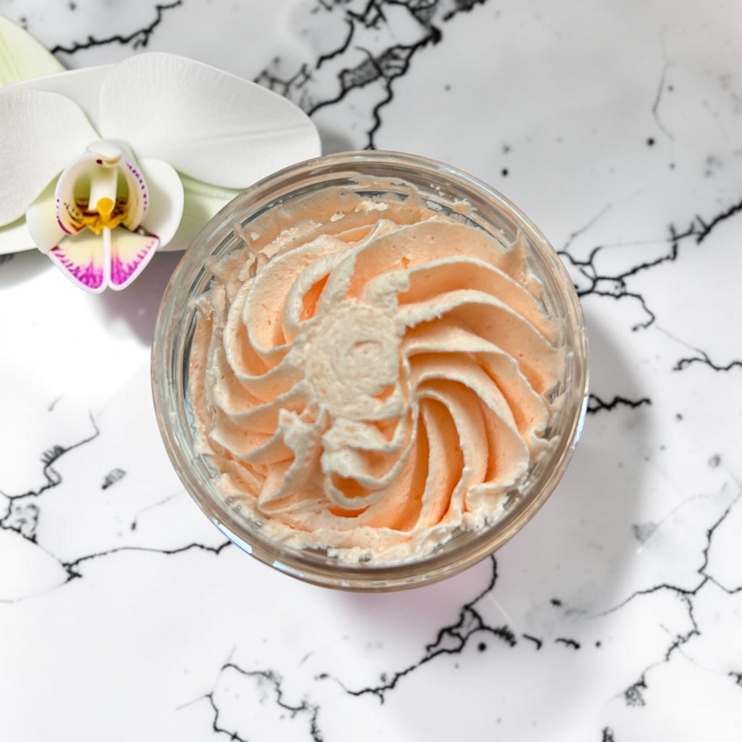 Doodlations Coffee Bar & Boutique Peachy Peach whipped soap in a jar with a swirl texture on a marble surface.