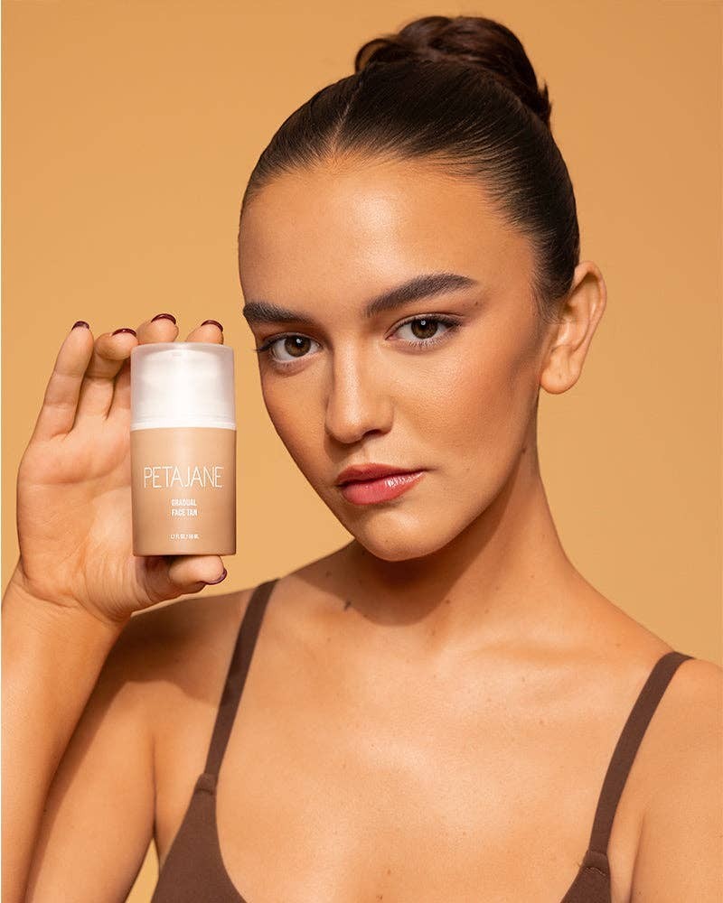 Model holding Doodlations Coffee Bar & Boutique Petajane Gradual Face Tan bottle for a natural sun-kissed glow.