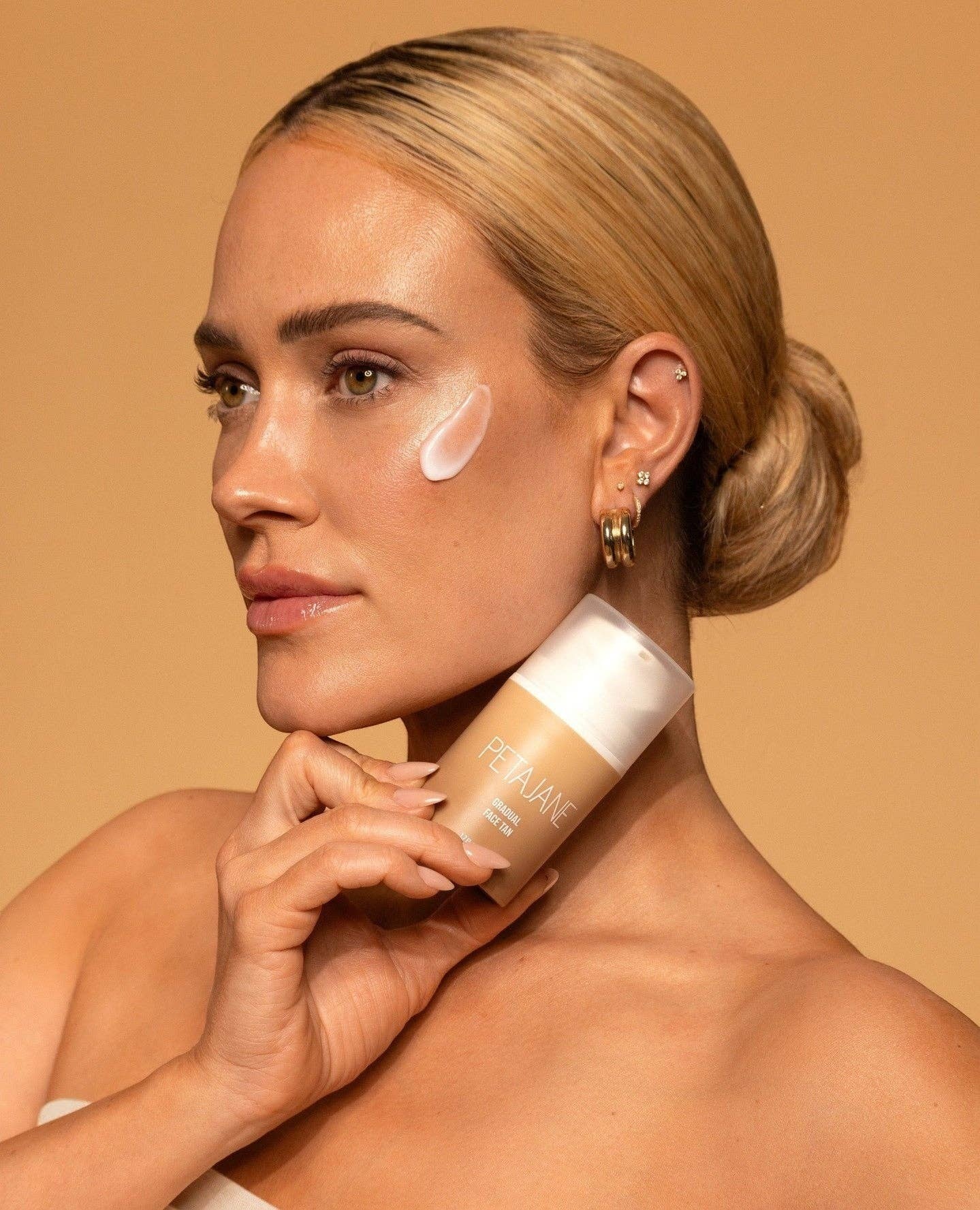 Model with glowing skin applying Doodlations Coffee Bar & Boutique Petajane Gradual Face Tan for a sun-kissed look.