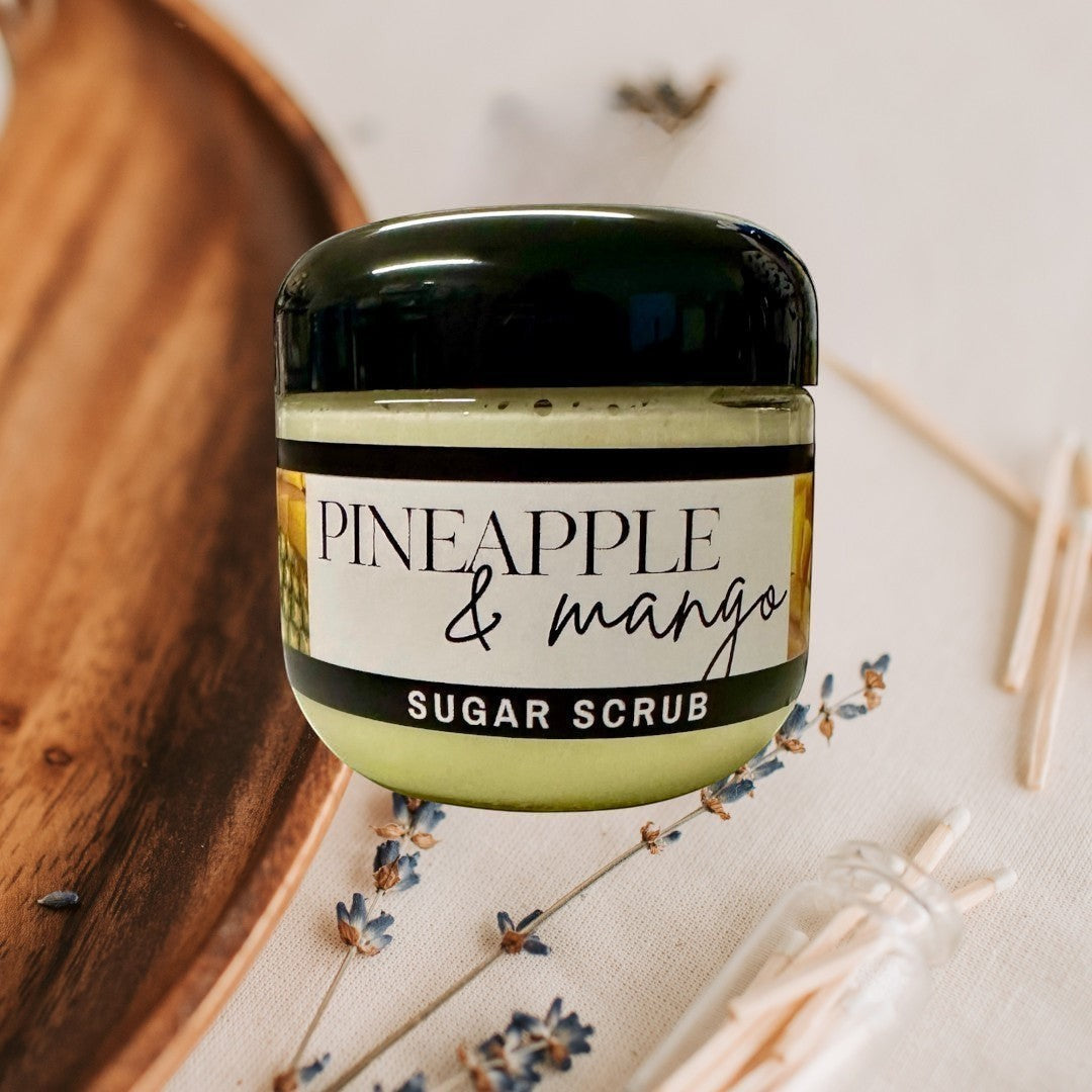 Doodlations Coffee Bar & Boutique Pineapple Mango Sugar Scrub, a pale yellow exfoliating scrub in a clear jar with a black lid.