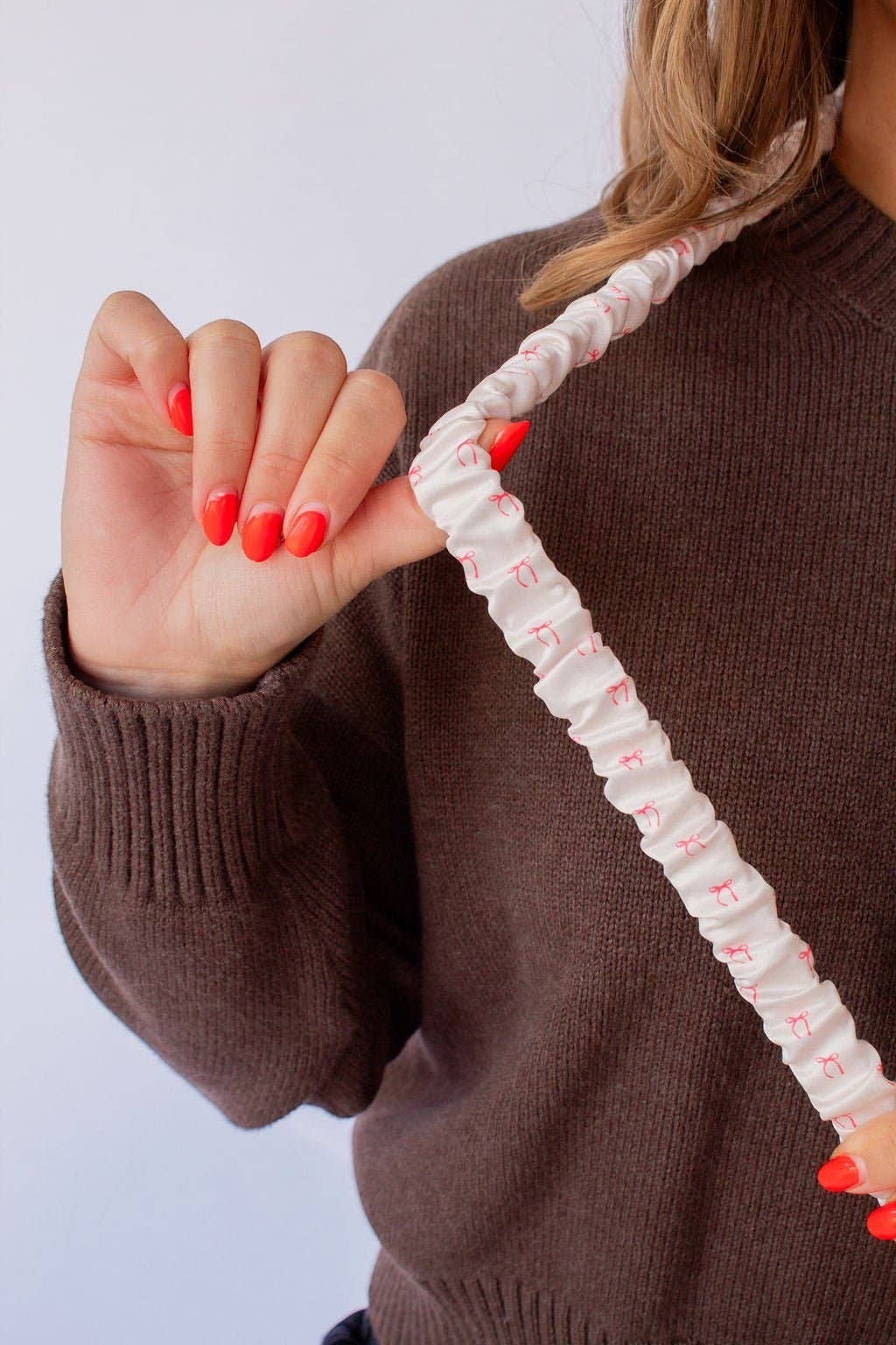 Doodlations Coffee Bar & Boutique pink bow patterned polyester lanyard worn by a person in a brown sweater