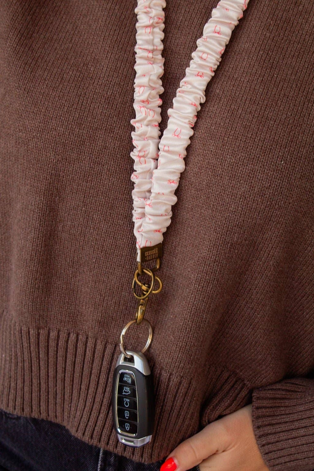 Doodlations Coffee Bar & Boutique pink bow print scrunchie lanyard with antique brass hardware holding car keys