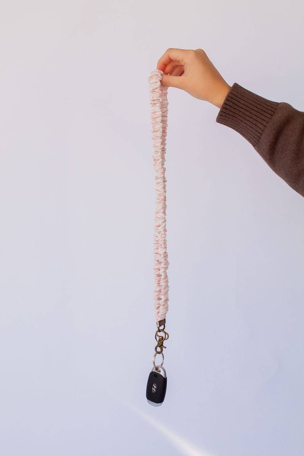 Doodlations Coffee Bar & Boutique pink bow print textured polyester lanyard held by a hand with a car key attached
