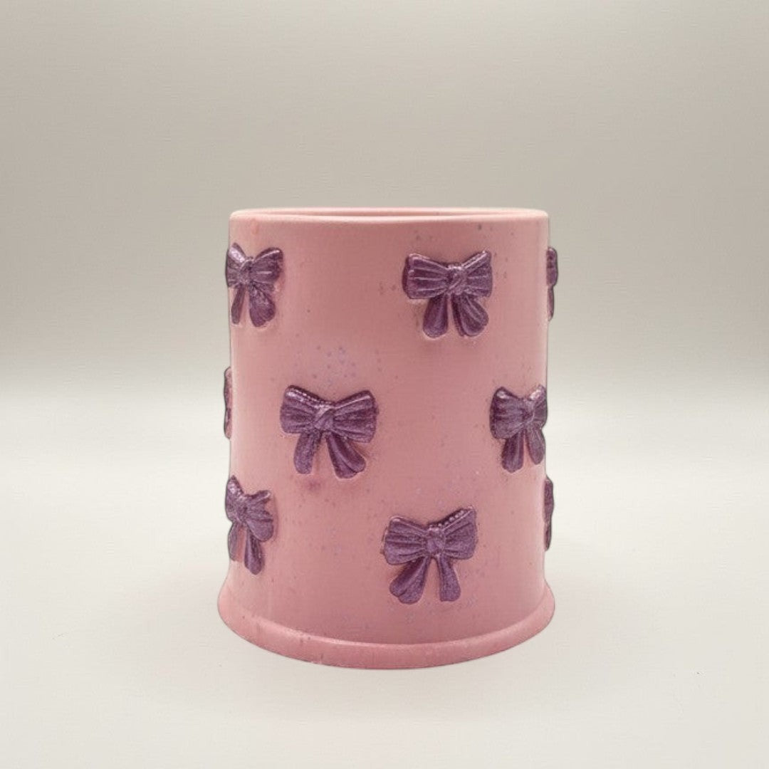 Doodlations Coffee Bar & Boutique pink concrete candle with purple bow accents and glitter flecks. 8oz soy blend wax.